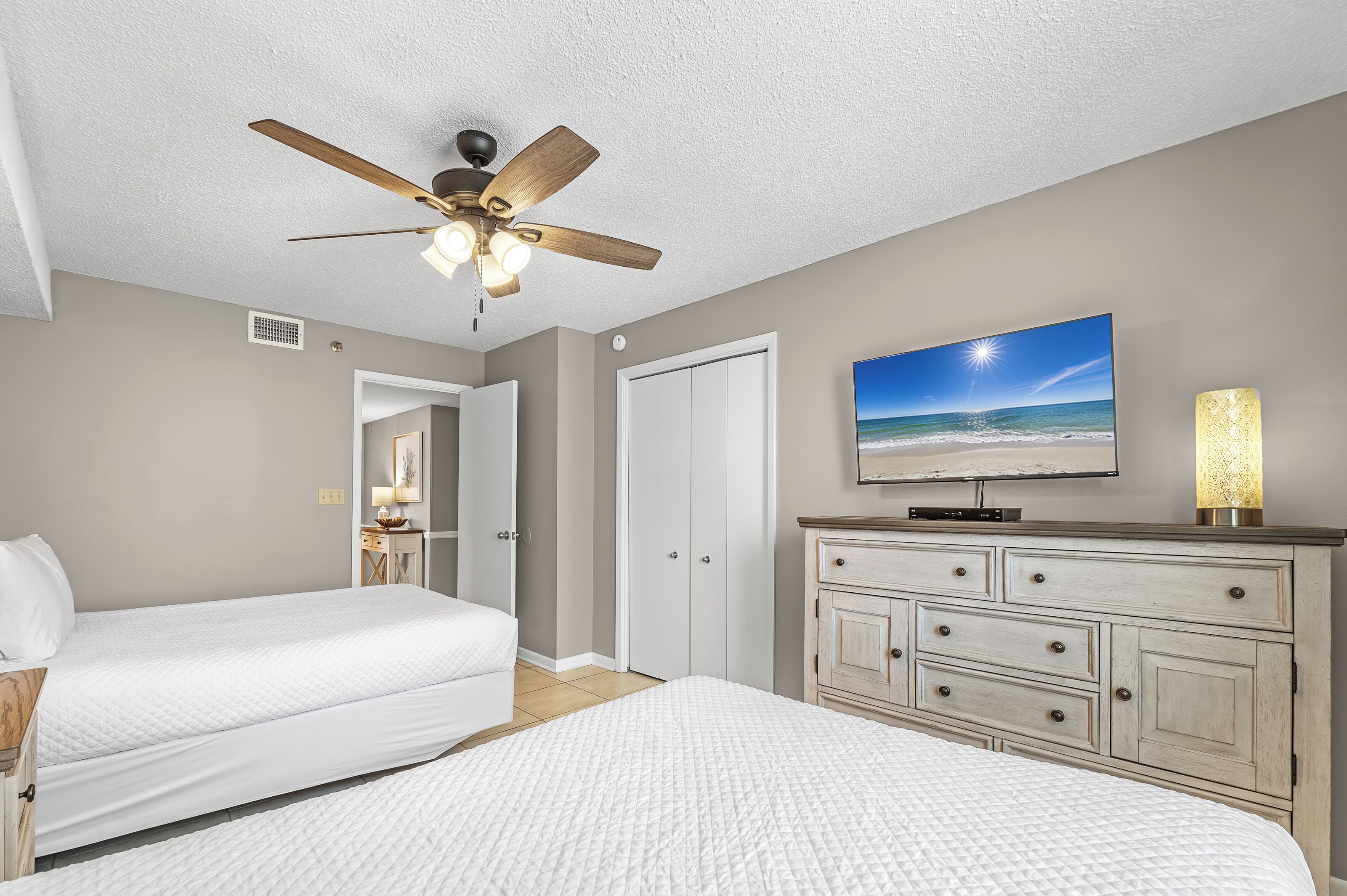 A bedroom with two beds, a ceiling fan, a TV, and a nightstand.