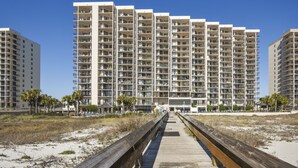 Een strandhotel met meerdere hoge gebouwen, een houten boardwalk naar het strand en palmbomen.