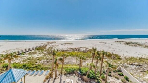 Uitzicht op een strand met een houten looppad, palmbomen en een gebouw met een blauw dak.