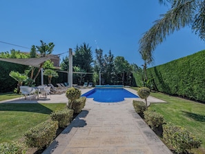 A swimming pool with a paved walkway leading to a seating area with chairs and a table.