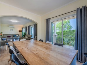 A spacious living area with a wooden dining table, sofas, and a balcony with curtains.