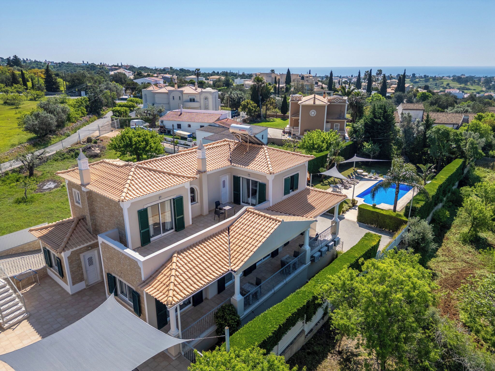 A large house with a swimming pool, surrounded by greenery and other houses.