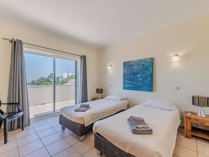Ett hotellrum med två sängar, ett skrivbord, en stol, en tavla och utsikt genom en skjutdörr.