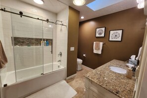 A modern bathroom with a glass-enclosed shower, a granite countertop sink, and two framed wall art pieces. - Completely remodeled Up North condo near clubhouse at Birchwood Farms (Harbor Springs)