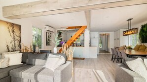 A spacious living area with a grey sofa set, a wooden staircase, and a dining area with a table and chairs. - L`Oasis Zen bord de L`eau, Spa,Foyer (Nominingue)