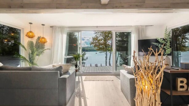 A modern living room with a large sliding glass door leading to a deck overlooking a lake. - L`Oasis Zen bord de L`eau, Spa,Foyer (Nominingue)