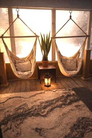 A cozy room with two hammocks, a potted plant, and a lantern on a wooden table. - L`Oasis Zen bord de L`eau, Spa,Foyer (Nominingue)