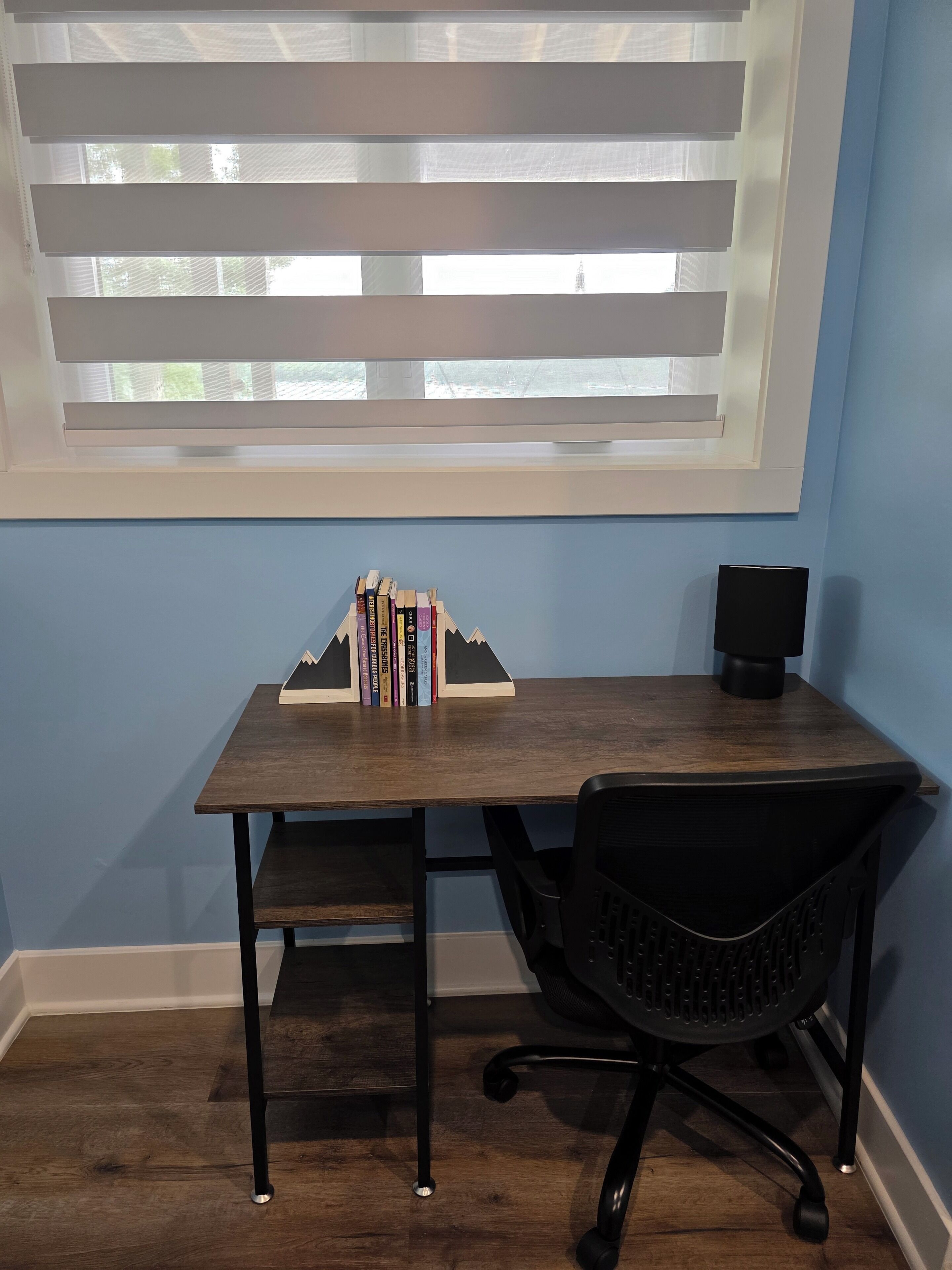 Una habitación con escritorio, silla y ventana con persianas.