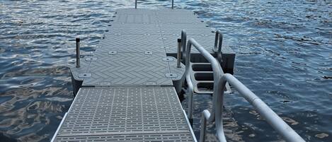 Un muelle de metal que se adentra en un lago tranquilo con un paisaje montañoso al fondo.