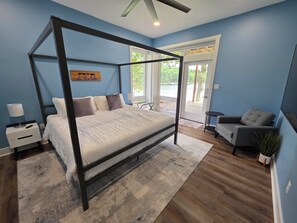 A bedroom with a four-poster bed, a nightstand, a chair, and a view of the outdoors.