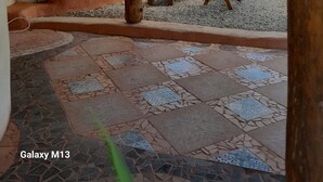 A covered outdoor area with a tiled floor, a wooden bench, a small table, and a large pot.