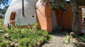 A dome-shaped building with a small window and a door, surrounded by greenery and a tree.