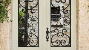A door with ornate black metalwork and two green glass bottles on a stone ledge. - Holiday home with air conditioning and internet (Grožnjan)