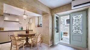A dining area with a round table and four chairs, a hanging light fixture, a kitchen area with cabinets and a window, and a door with decorative ironwork. - Holiday home with air conditioning and internet (Grožnjan)