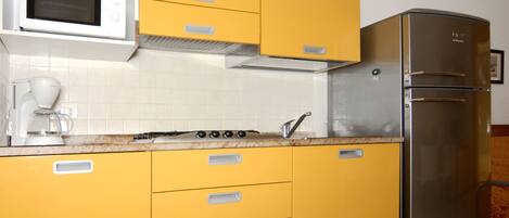 Une cuisine avec des meubles de couleur jaune, un réfrigérateur en acier inoxydable, un four à micro-ondes et une cuisinière.