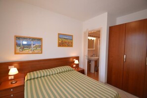 A bedroom with a bed, nightstands, a wooden wardrobe, a bathroom with a sink, and two framed pictures on the wall.