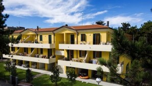 A yellow building with a red roof, multiple balconies, and a parking area. - Lovely Flat in a Building Surrounded by Garden (San Michele al Tagliamento)
