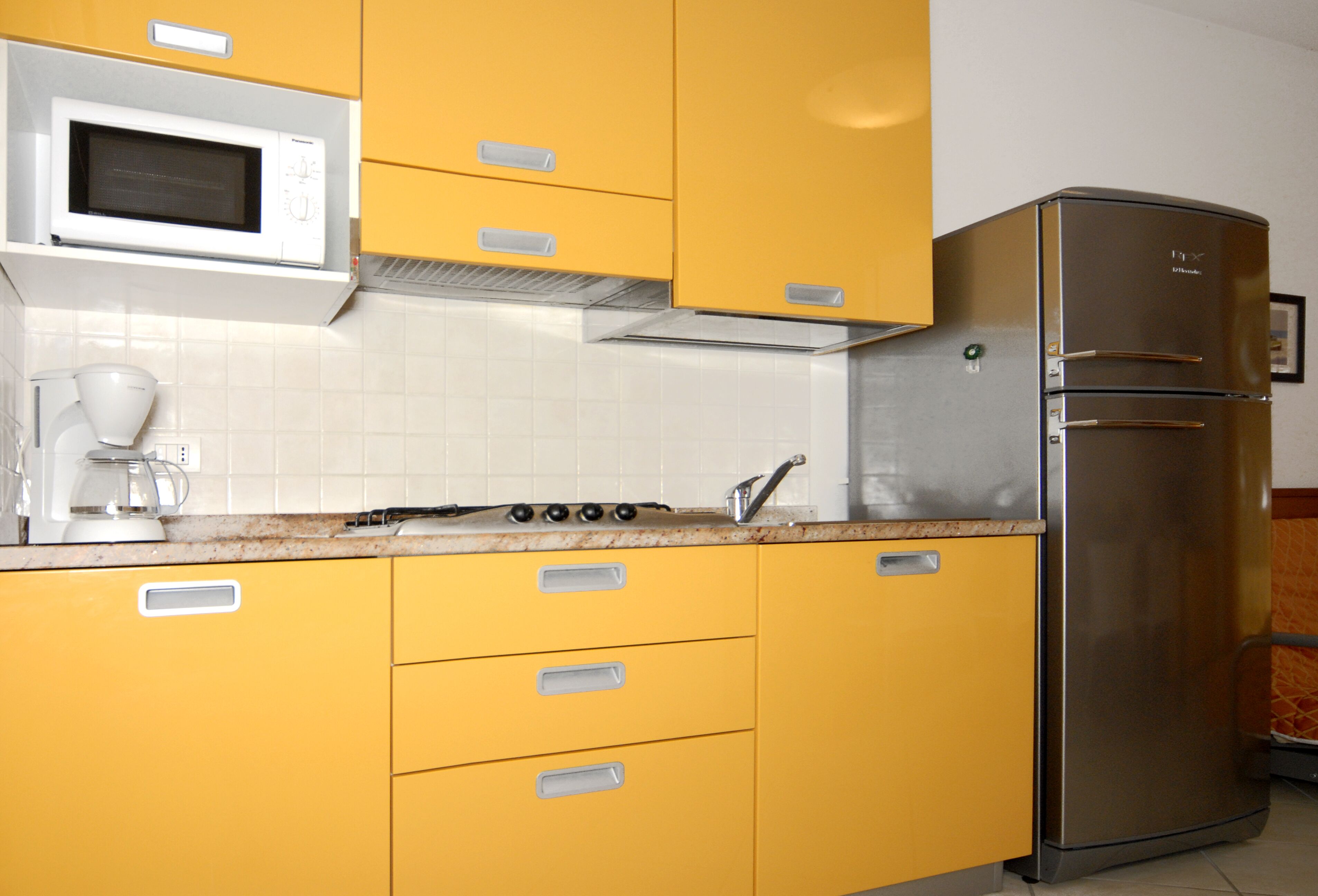 A kitchen with yellow cabinets, a stainless steel refrigerator, a microwave, and a stove.