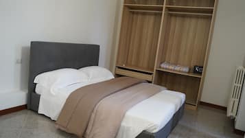 A bedroom with a bed, a grey headboard, a wooden wardrobe, and a radiator.