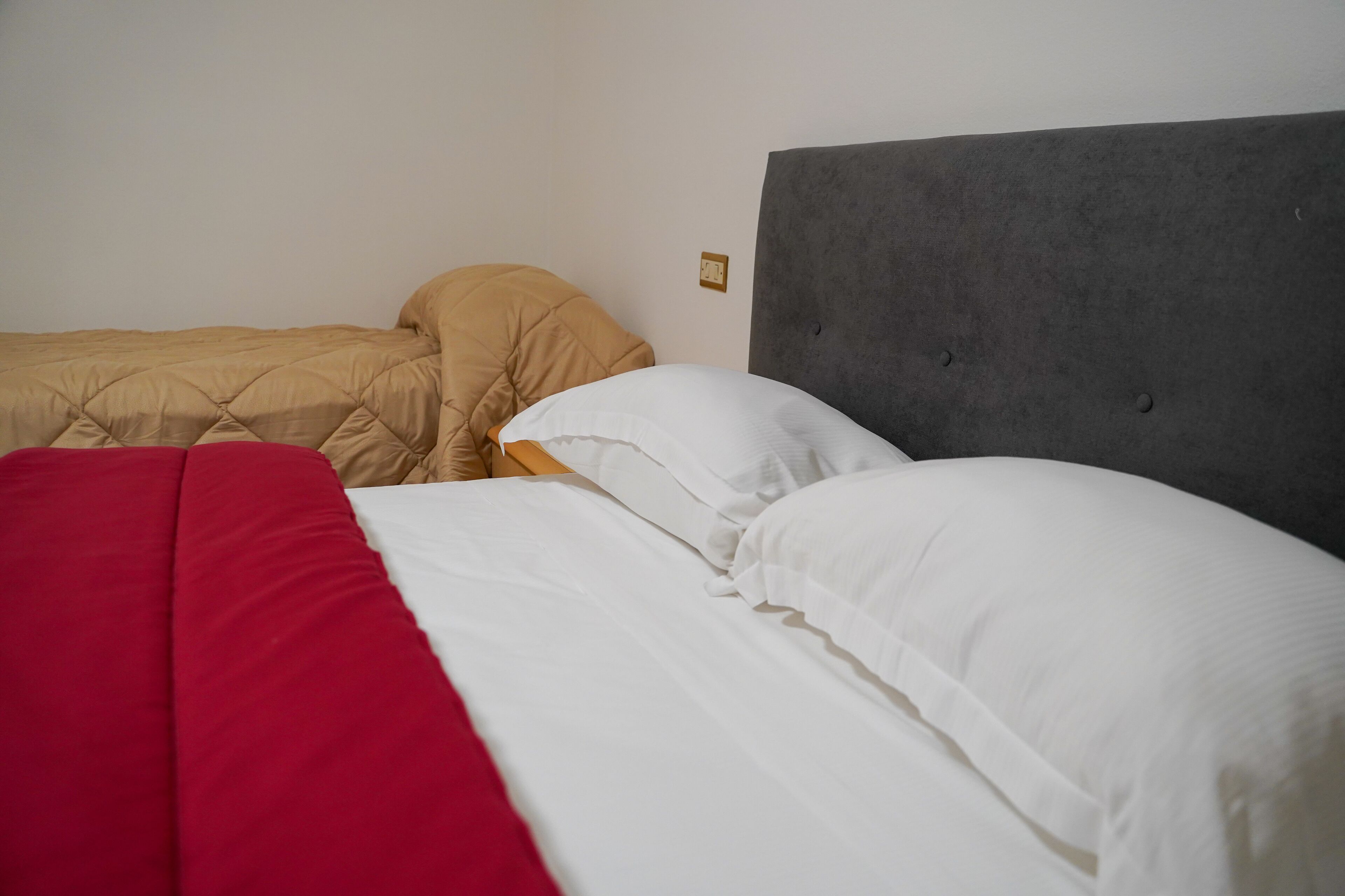 A hotel room with two beds, one with a red and white bedspread and the other with a beige and white bedspread.