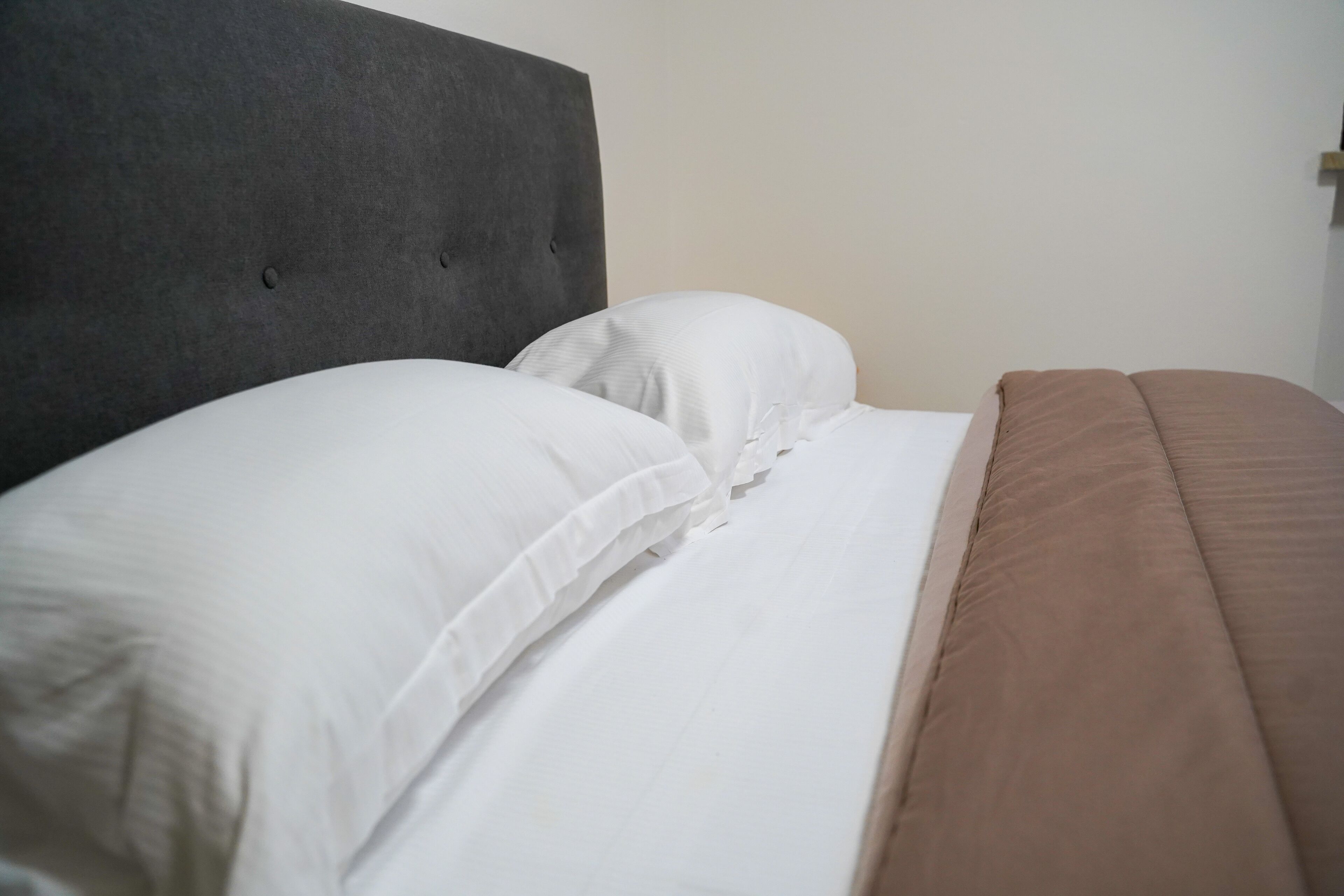 A bed with a grey headboard, white pillows, and a brown blanket.