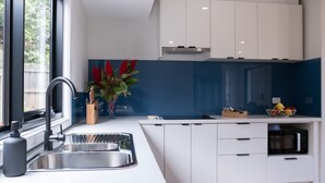 A modern kitchen with white cabinets, a stainless steel sink, and a blue backsplash. - Moon Pot at Waters Edge (Mount Martha)