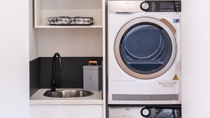 A compact laundry room with a washing machine, dryer, and a shelf with a Monopoly game. - Moon Pot at Waters Edge (Mount Martha)