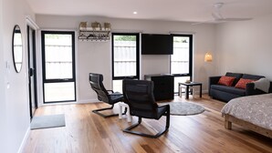 A modern living room with a bed, two chairs, a TV, and a ceiling fan. - Moon Pot at Waters Edge (Mount Martha)