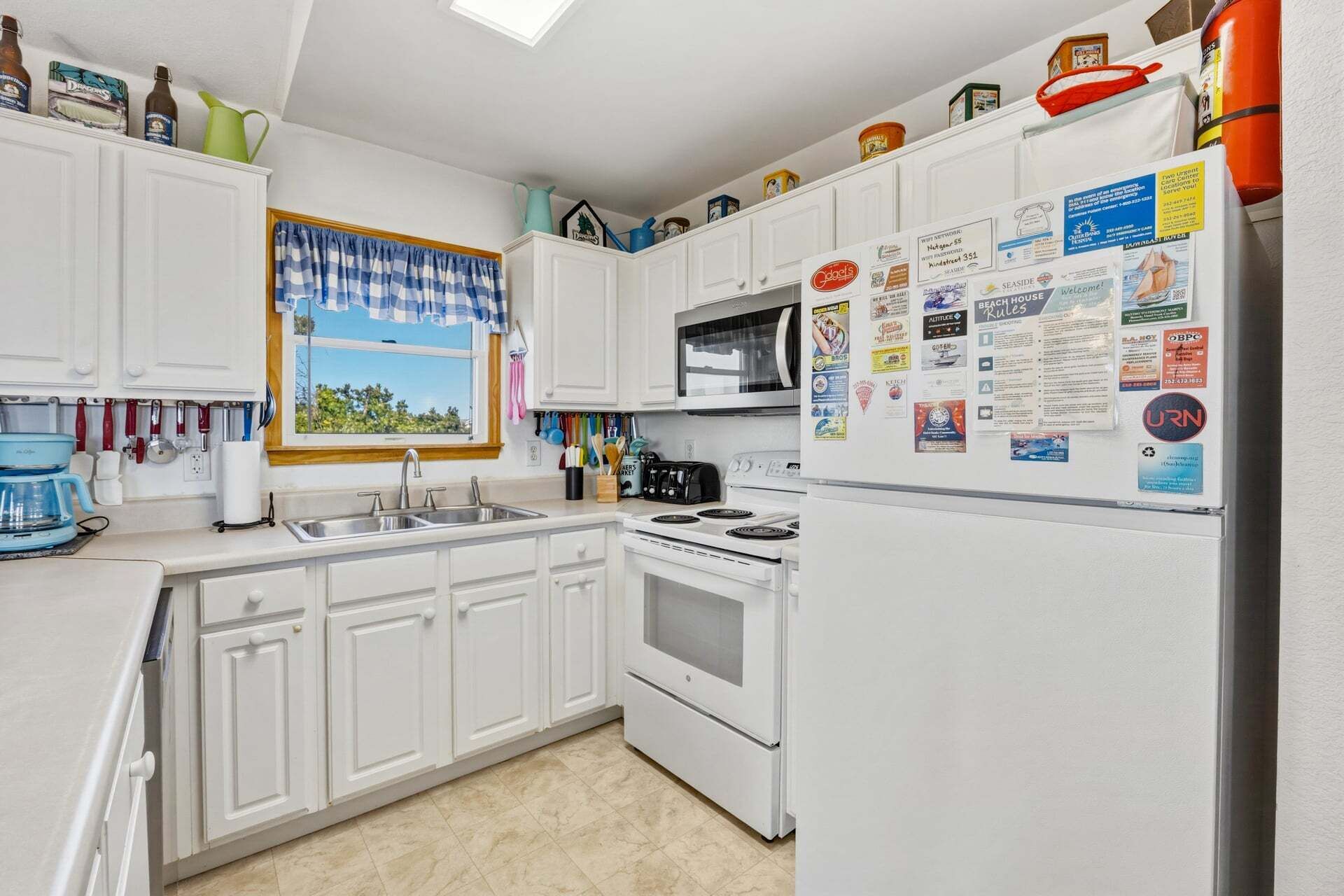A kitchen with white cabinets, a stove, a sink, and a refrigerator covered in various notices.