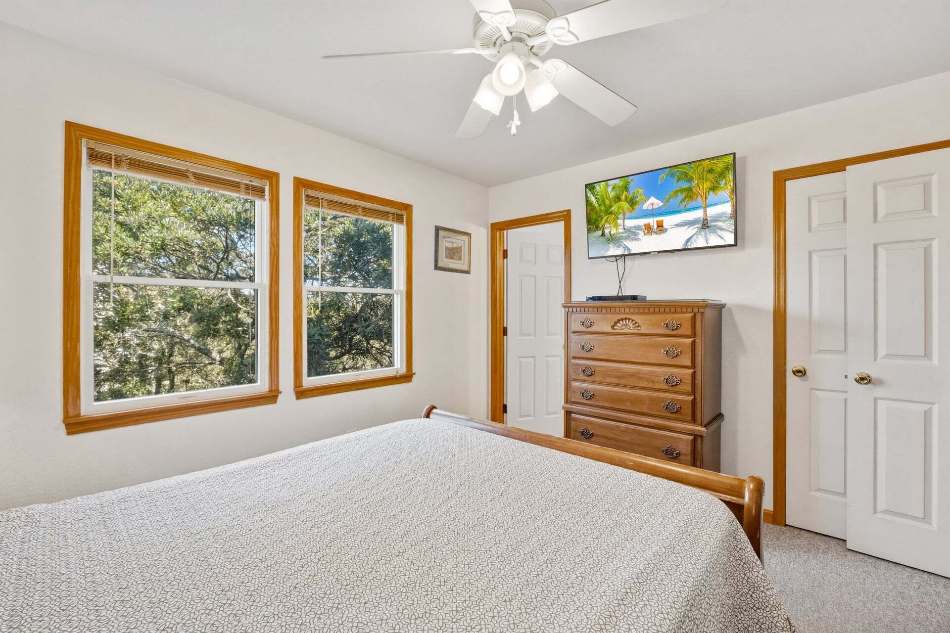 A bedroom with a bed, a dresser, a ceiling fan, and a TV on the wall.