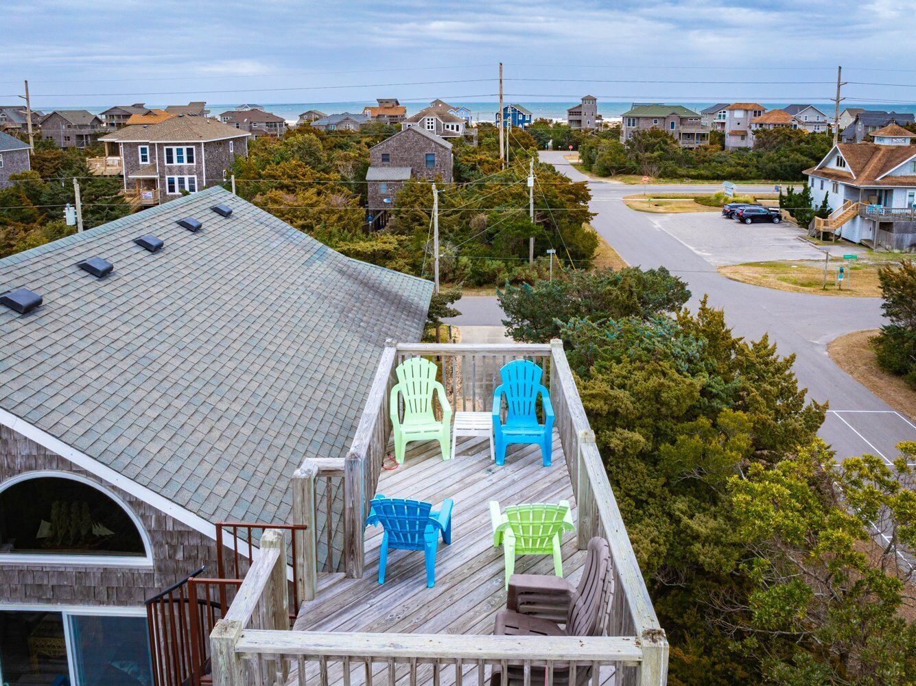 A residential area with a wooden deck featuring Adirondack chairs and a view of the ocean.
