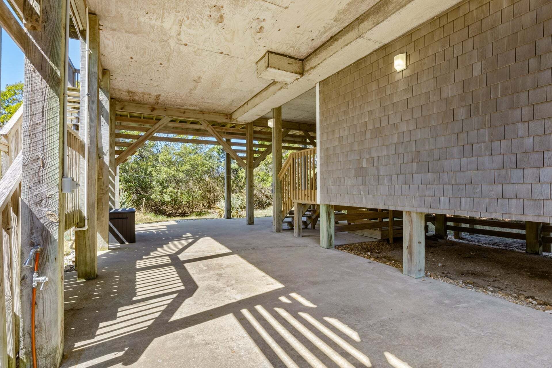 A covered outdoor area with a concrete floor, wooden beams, and a brick wall.