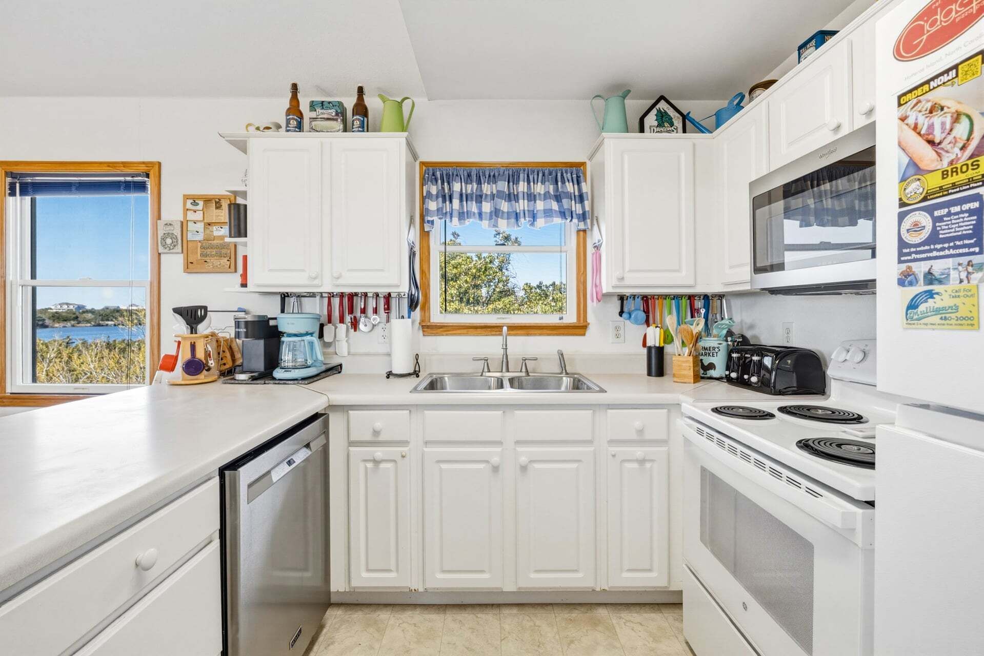 Een keuken met witte kasten, een fornuis, een spoelbak en een raam met uitzicht.