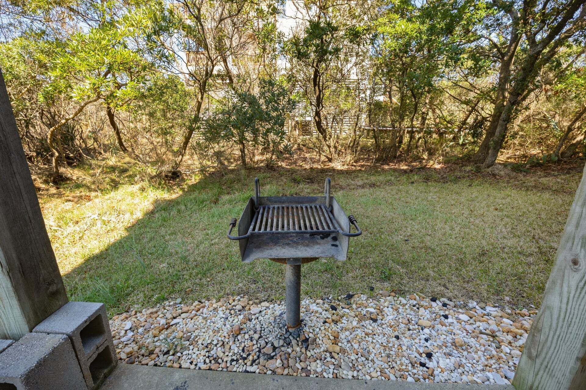 A barbecue grill in a grassy area with trees in the background.