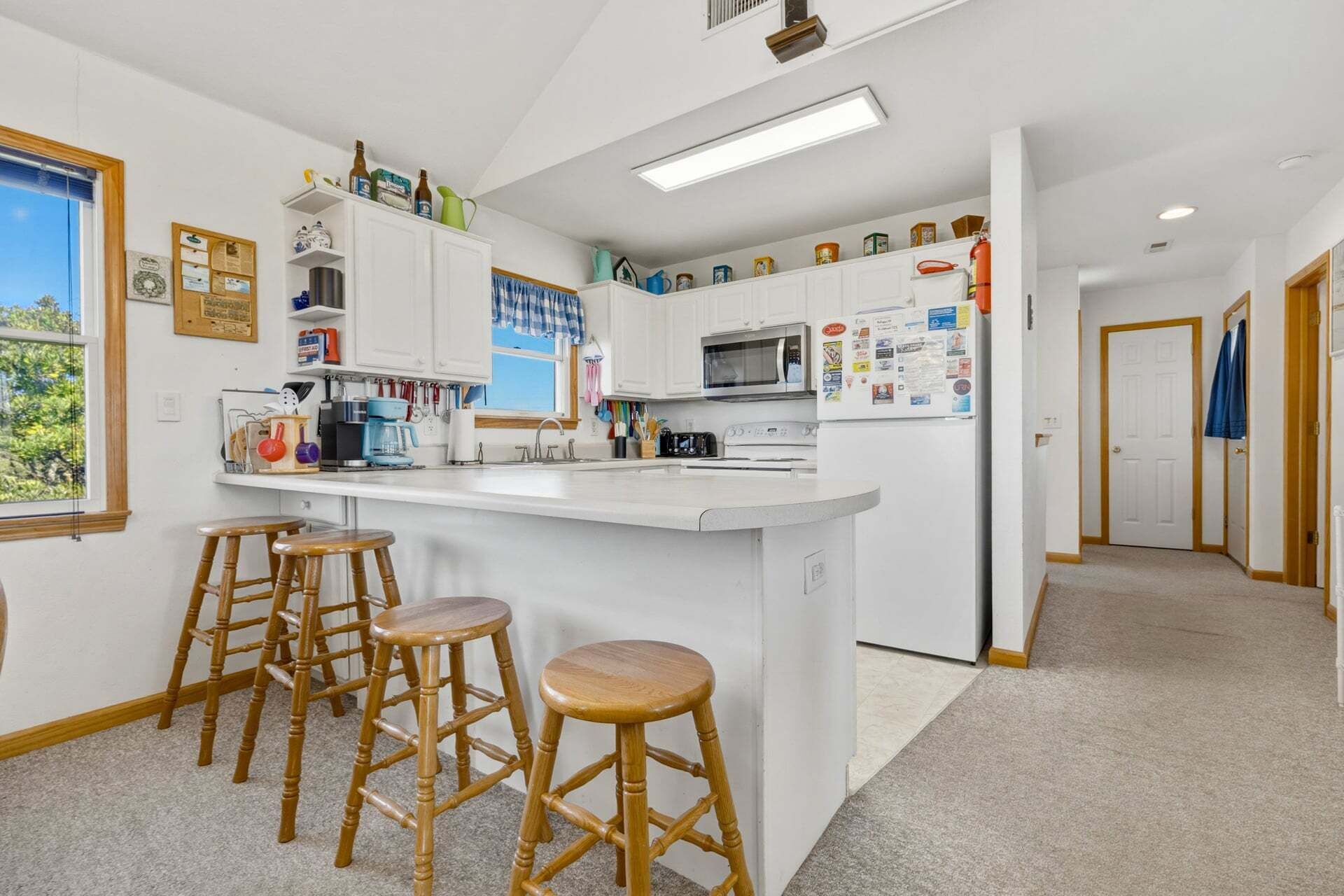 A modern kitchen with white cabinets, a central island with stools, a microwave, and a refrigerator.