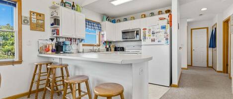 A modern kitchen with white cabinets, a central island with stools, a microwave, and a refrigerator.