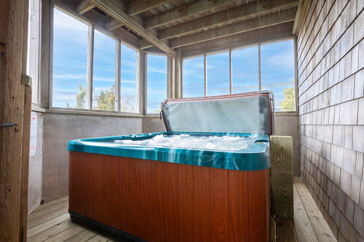 A hot tub in a wooden room with large windows and a view of the outdoors.
