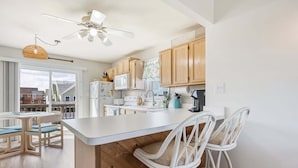 A kitchen with wooden cabinets, a white island with bar stools, a ceiling fan, and a view of the outside.