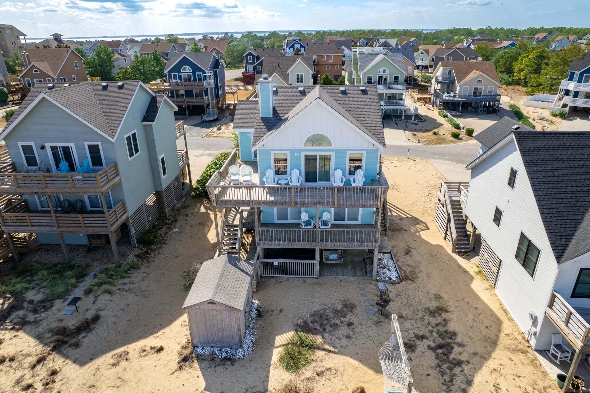 A residential area with houses featuring balconies, a sandy ground, and a clear sky.