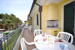A balcony with a table set for dining, a grill, and a view of the surrounding area.