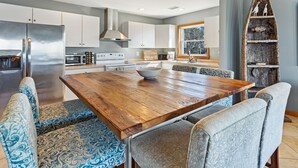 Een moderne keuken met witte kastjes, roestvrijstalen apparatuur en een houten eettafel met gestreept beklede stoelen.