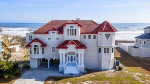 A large, two-story house with a red-tiled roof, a front entrance with steps, and a view of the ocean. - Carpe Diem Corolla OBX  Pool HotTub (Corolla)
