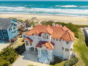 A large, two-story house with a red-tiled roof, located near a beach with ocean views.
