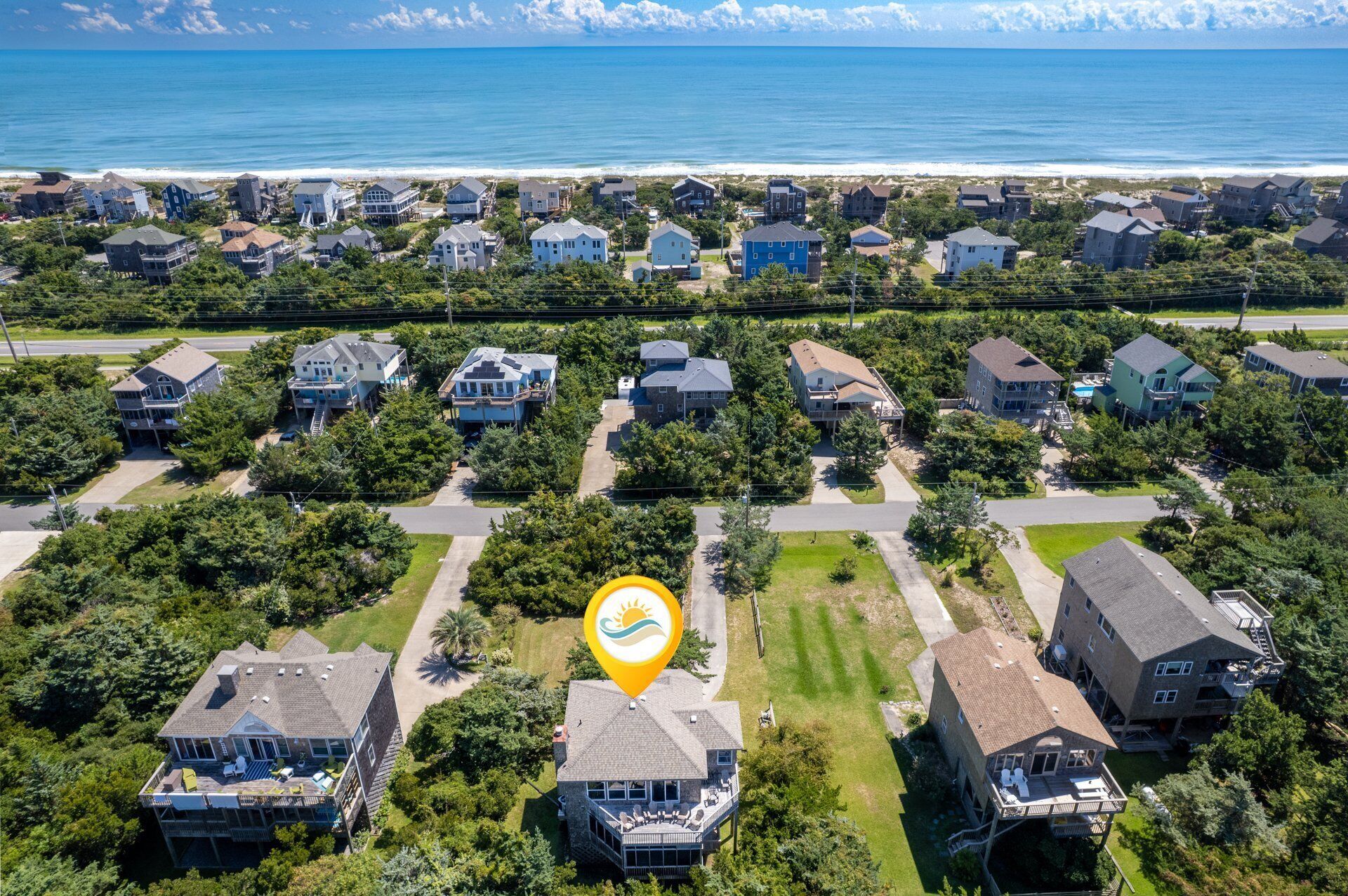 An aerial view of a coastal residential area with houses, a beach, and a marked location.
