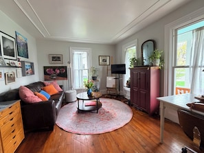 A living room with a brown leather sofa, a round rug, a wooden coffee table, a TV stand, and a cabinet.