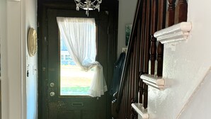 Uma escada de madeira com corrimão branco, uma porta escura com janela e um candelabro.