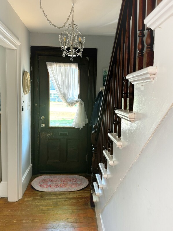 A wooden staircase with a white handrail, a dark door with a window, and a chandelier. - Charming Village Home with an Enchanting Backyard Oasis (Geneseo)