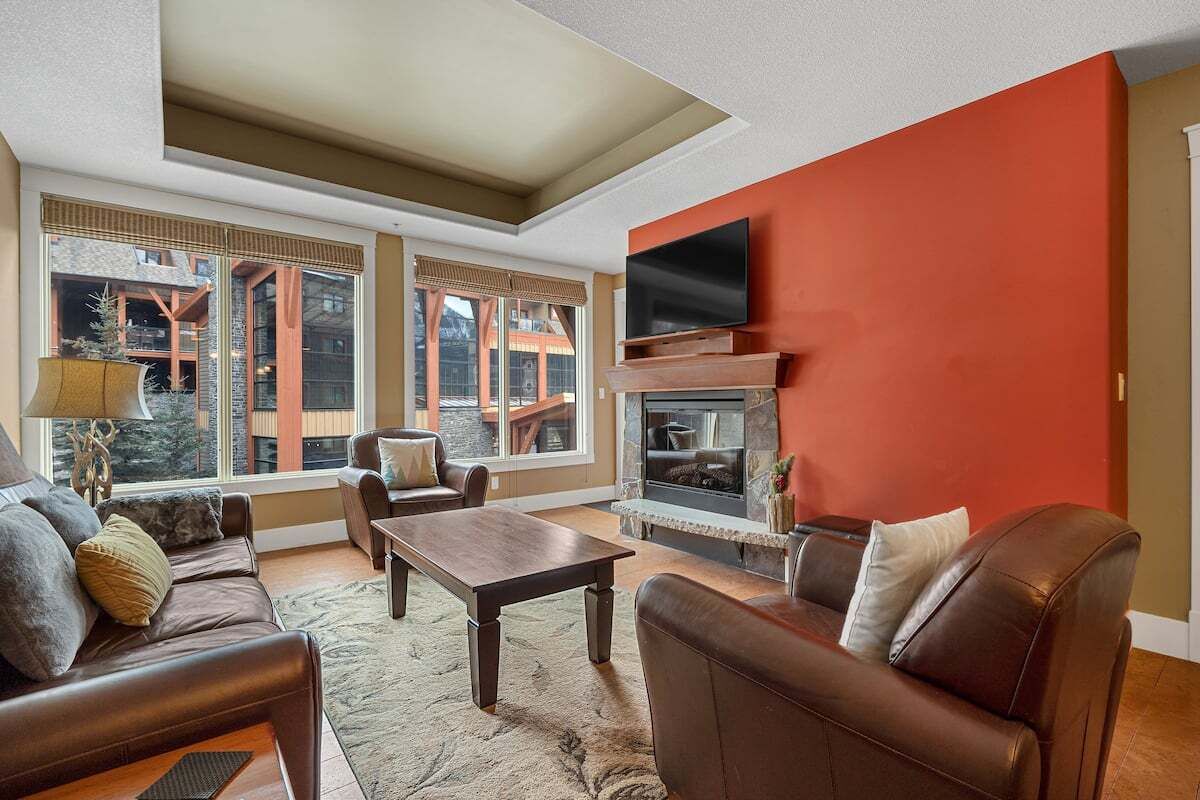 A modern living room with a fireplace, leather sofas, a coffee table, and large windows offering a view of the outside.