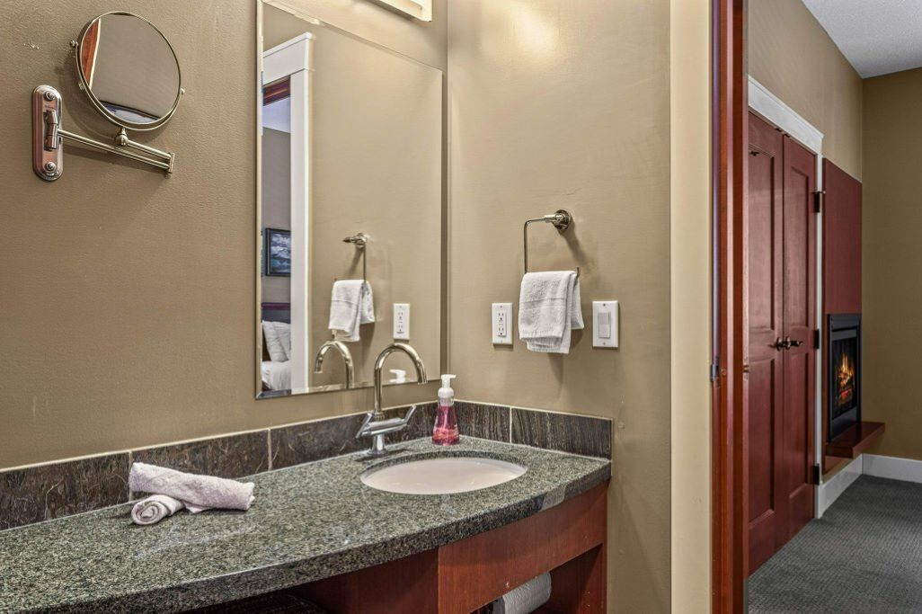 Un baño de hotel con lavamanos de encimera de granito, espejo, toallero y chimenea.