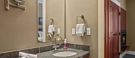 Un baño de hotel con lavamanos de encimera de granito, espejo, toallero y chimenea.